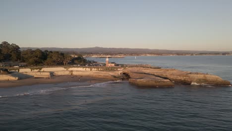 Golden-hour-circular-drone-shot-featuring-Lighthouse-Point-on-a-peninsula,-Santa-Cruz,-California