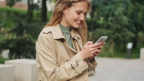 caucasian female student using smartphone and smiling outdoors.