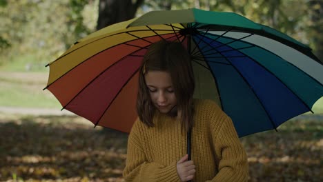 Caucasian-girl-walking-across-the-park-with-colorful-umbrella.