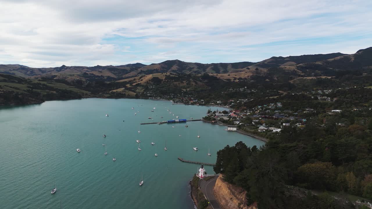 Anchored yachts and boats at beach of akaroa town. Canterbury Region, new Zealand . Aerial wide shot. Lighthouse and French bay