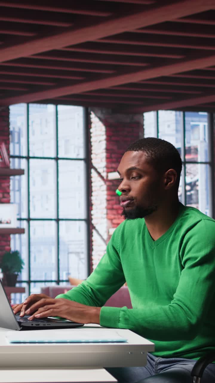 Vertical Video Focused male freelancer browsing web on laptop in a modern studio loft