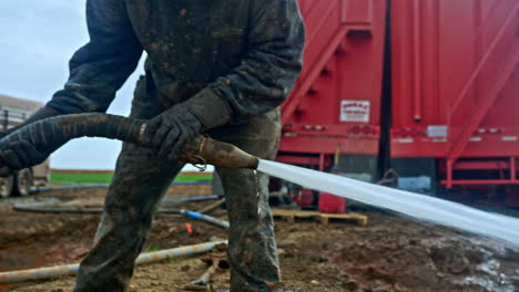 unrecognized man in dirty clothes holding a hose with water flowing from it. two red trucks at backdrop. oil or gas production.