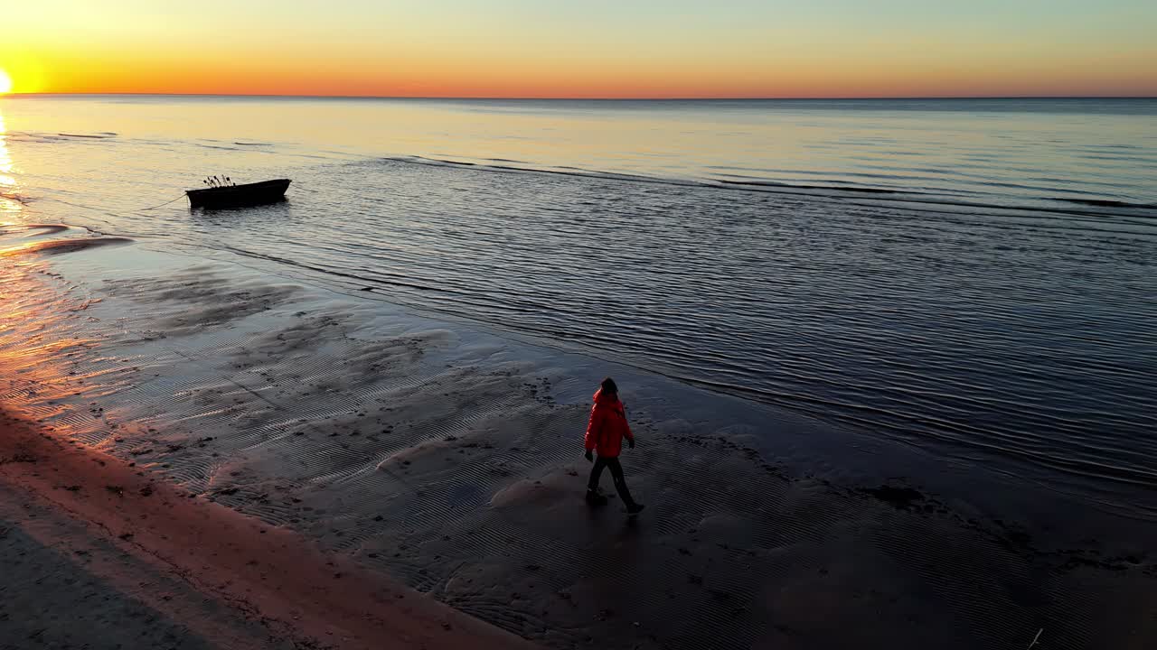 Una persona con giacca rossa cammina sulla spiaggia al tramonto