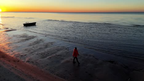 Eine-Person-In-Einer-Roten-Jacke-Geht-Bei-Sonnenuntergang-Am-Strand-Spazieren