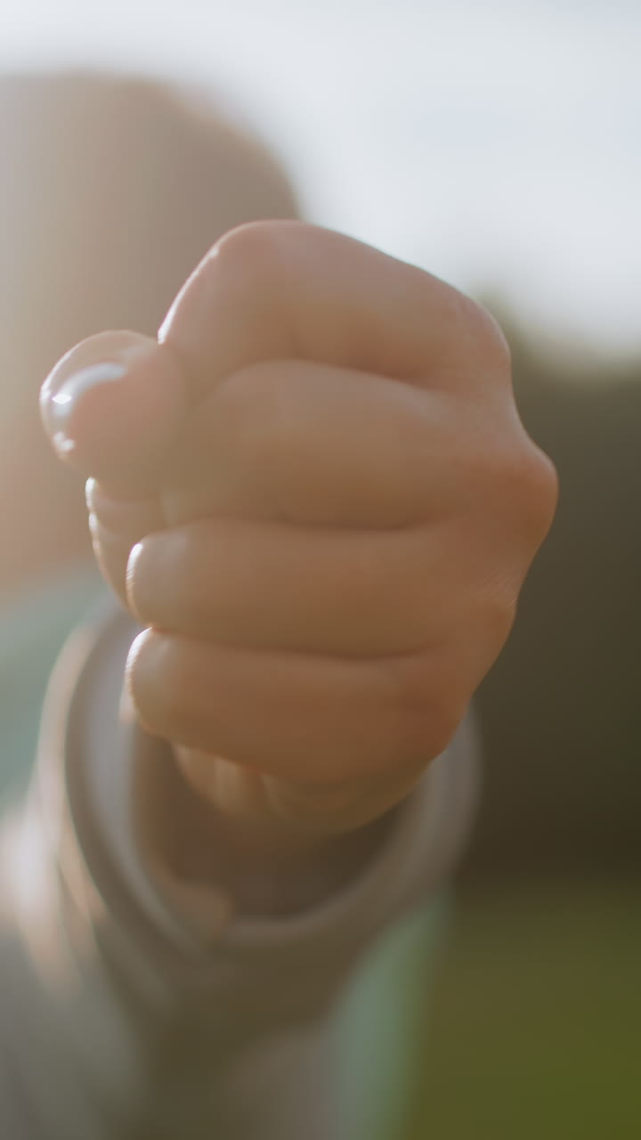 Primer plano de un puño apuntando hacia la cámara con luz solar en el borde, textura de la piel y manicura visibles, agarre firme y energía concentrada, fondo exterior, transmite empoderamiento, mando e intención motivacional.