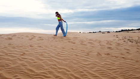 Paisaje-Escénico-De-Dunas-De-Arena-Roja,-Joven-Actriz-Caminando-En-Un-Entorno-Natural-Con-Ropa-Moderna-De-Moda