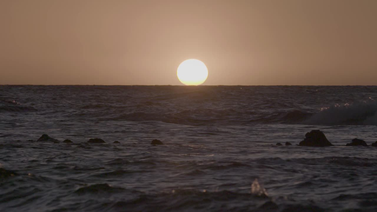 Looking out onto the ocean as waves roll across the setting sun in Hawaii