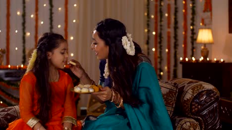 indian mother and daughter in tradtional dress during the festival celebration - mother feeding sweets to her daughter