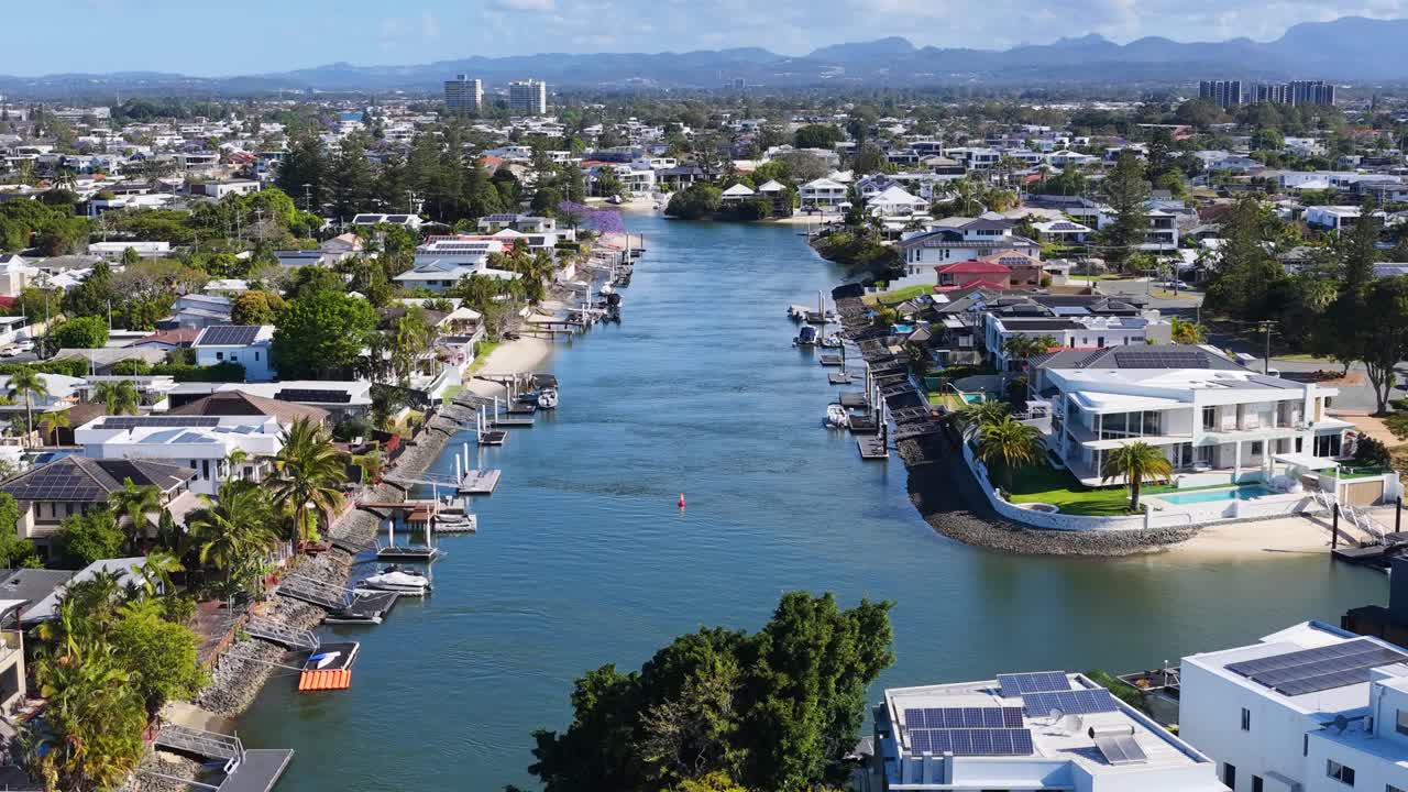 Sunny daytime drone footage gliding above residential canal, waterfront houses, and distant city skyline
