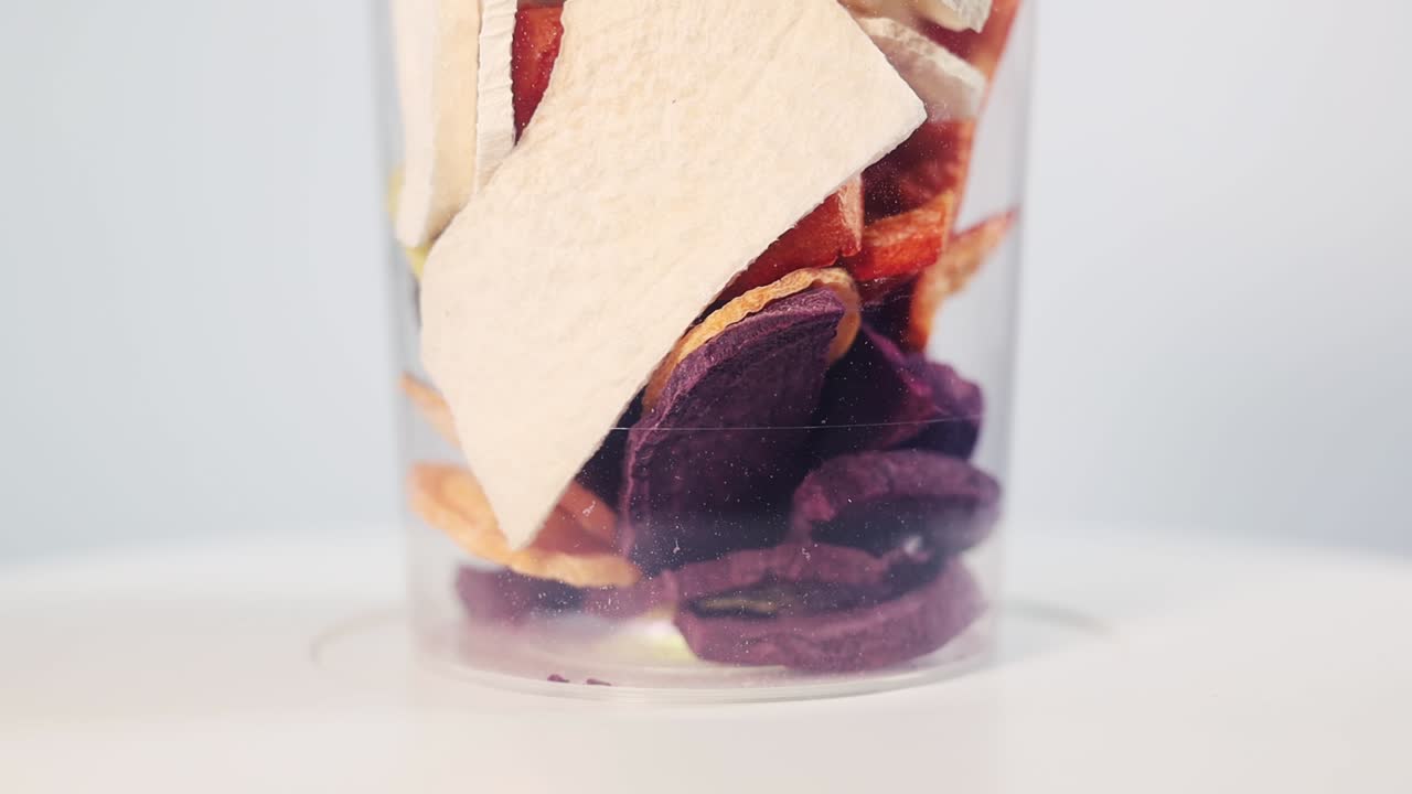 A transparent plastic container filled with colorful slices of freeze-dried carrots and beets, showcasing their vibrant orange, yellow, and purple hues. Ideal for snacking or cooking.