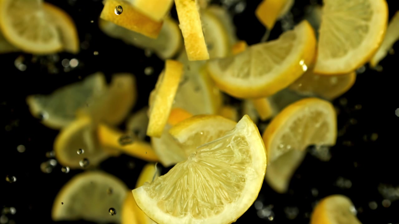 Fette di limone fresche che cadono al rallentatore con goccioline d'acqua