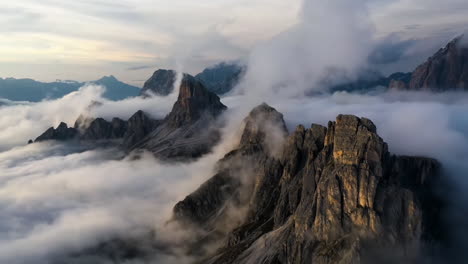 Drone-hyperlapse-of-low-hanging-clouds-moving-over-rocky-peaks,-sunrise-in-Dolomites,-Italy