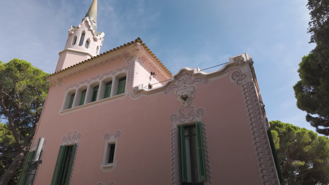 A pink building with decorative windows and greenery in Park Güell, Barcelona, Spain