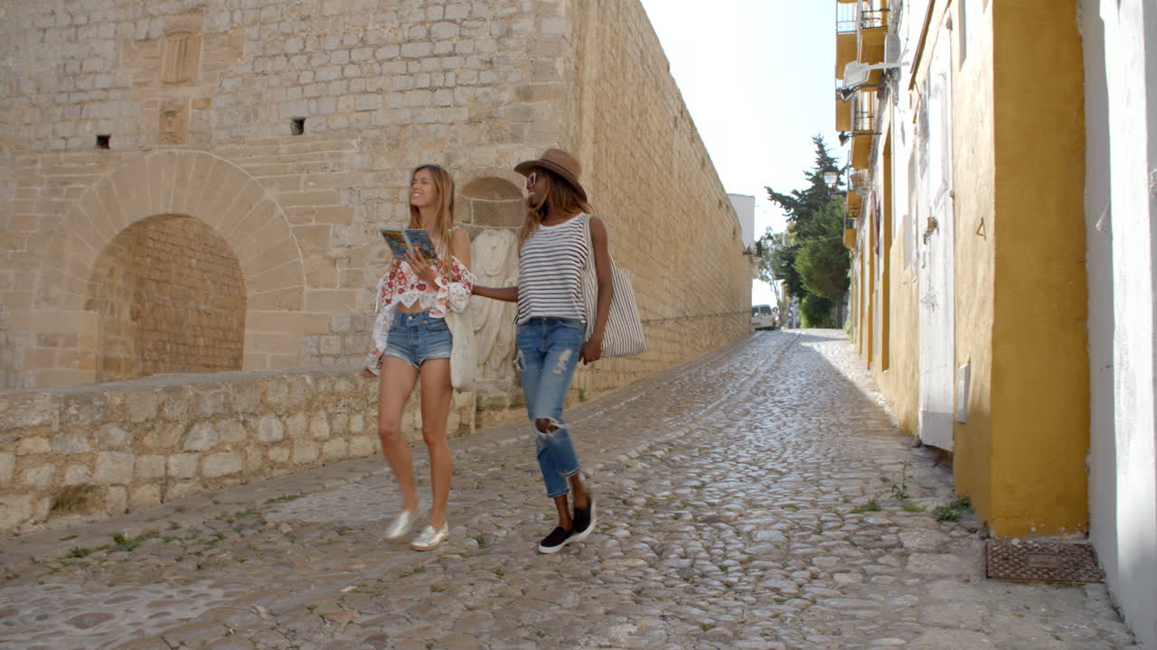 두 여인 친구 가 가이드북 을 들고 오래된 이비자 를 걸어다니고 있다