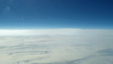 incredible view from the cockpit of an airplane flying high above the clouds leaving a long white condensation vapour air trail in the blue sky