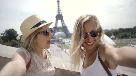 dos mujeres jóvenes tomando selfies en la ciudad de parís usando teléfonos móviles