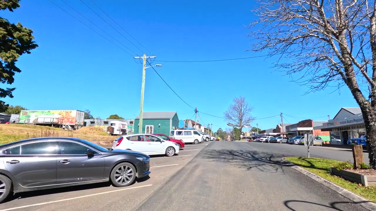 スタンソープの晴れた通りを、駐車された車や地元の店先を通り過ぎて車両が走行する。