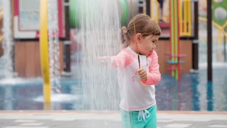 Niña-Divertida-De-3-Años-Lavándose-La-Mano-Bajo-Una-Ducha-Al-Aire-Libre-En-El-Parque-Acuático---Cámara-Lenta