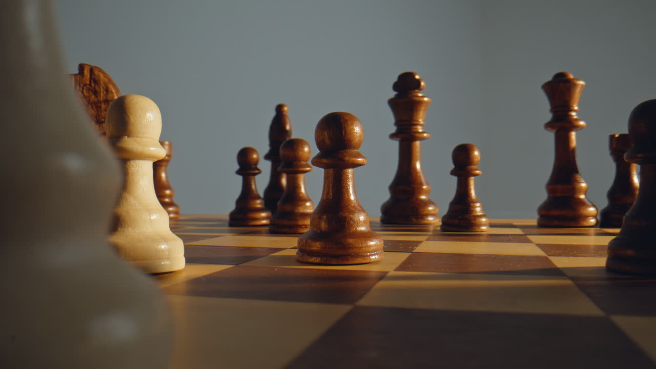 Hand moving white pawn on chessboard surrounded dark wooden chess pieces closeup