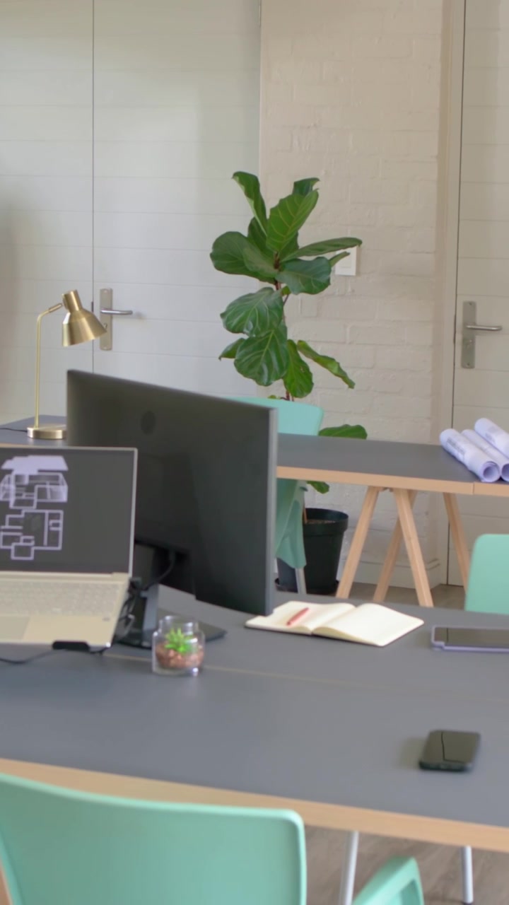Video verticale: Telecamera che panoramica rivelando scrivania, laptop e planimetria nell'ufficio di casa per mostrare lo spazio di lavoro.