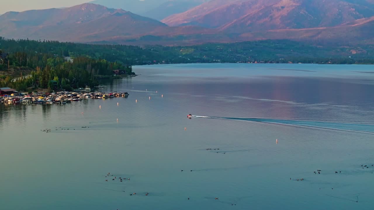 Drone aerial around boat approaching harbor at Grand Lake Colorado showing turquoise water and mountain slopes under soft afternoon light