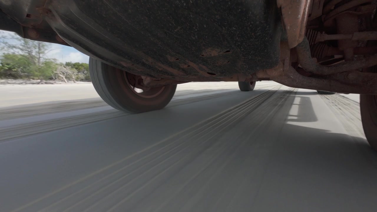 Vista POV (punto de vista) del tren de rodaje montada debajo de un vehículo 4x4 conduciendo por una playa remota y desierta en Cape York, Australia. Concepto de aventura todoterreno, conducción en playa y viaje por tierra.