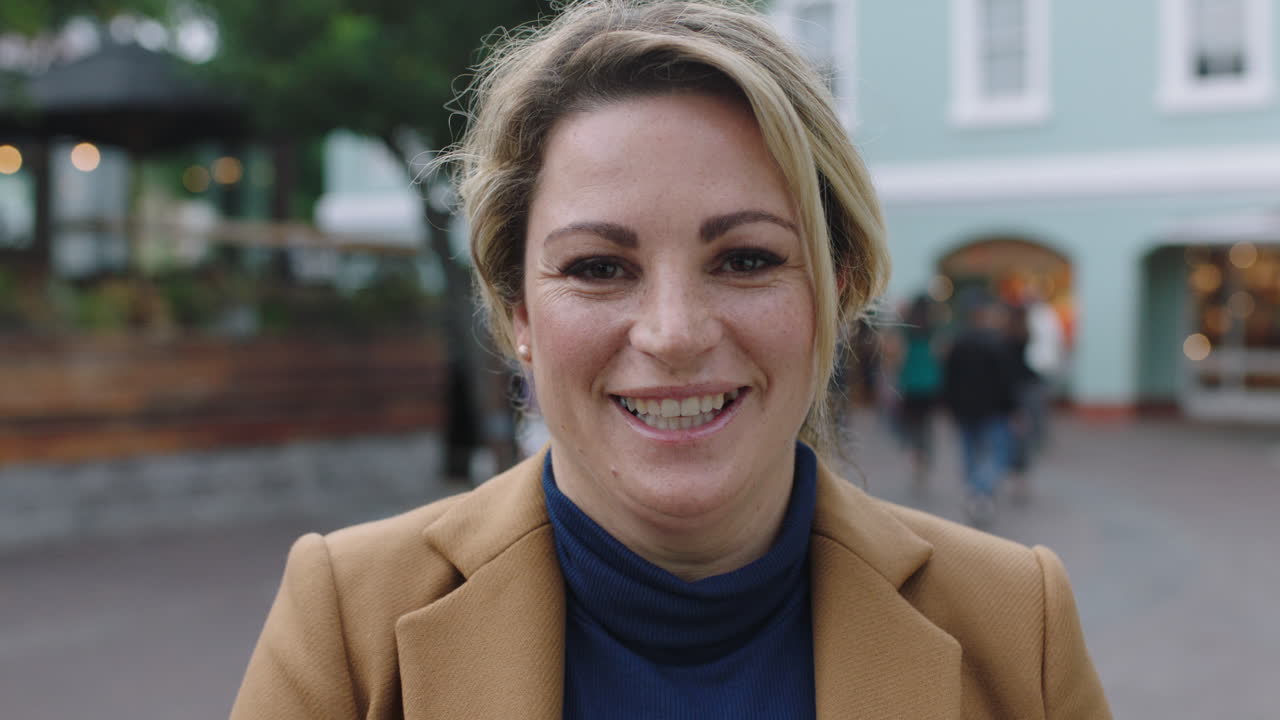 retrato en cámara lenta de una elegante mujer de negocios rubia en traje riendo alegremente ante la cámara de fondo urbano