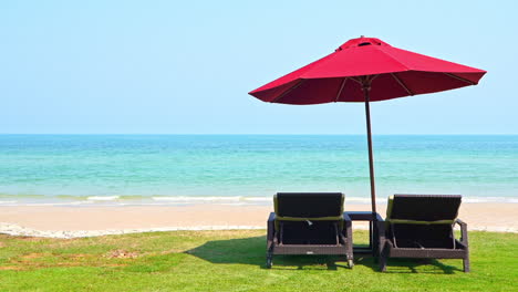 Two-empty-sun-loungers-sit-under-a-shade-umbrella-facing-the-incoming-waves