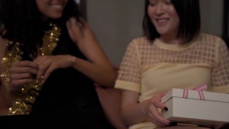 young woman gives a gift box with bow to her black female friend