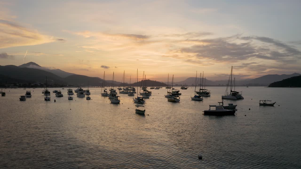 aérea cerca del agua distanciándose de yates, barcos y veleros anclados cerca de una costa brasileña en una hermosa puesta de sol