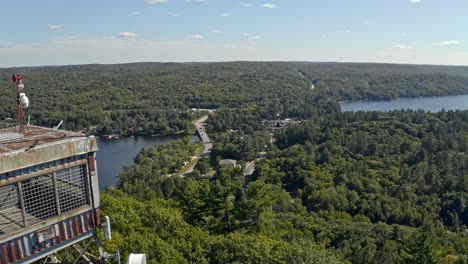 time lapse drone shot approaching fire lookout tower over lake with boats and cars driving in village in background