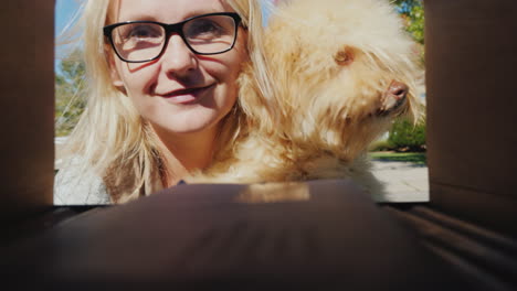 a young woman with a small dog in her arms picks up letters from a mailbox