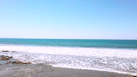 beautiful aerial drone footage with waves crashing on punta islita beach with blue skies in costa rica, pacific ocean