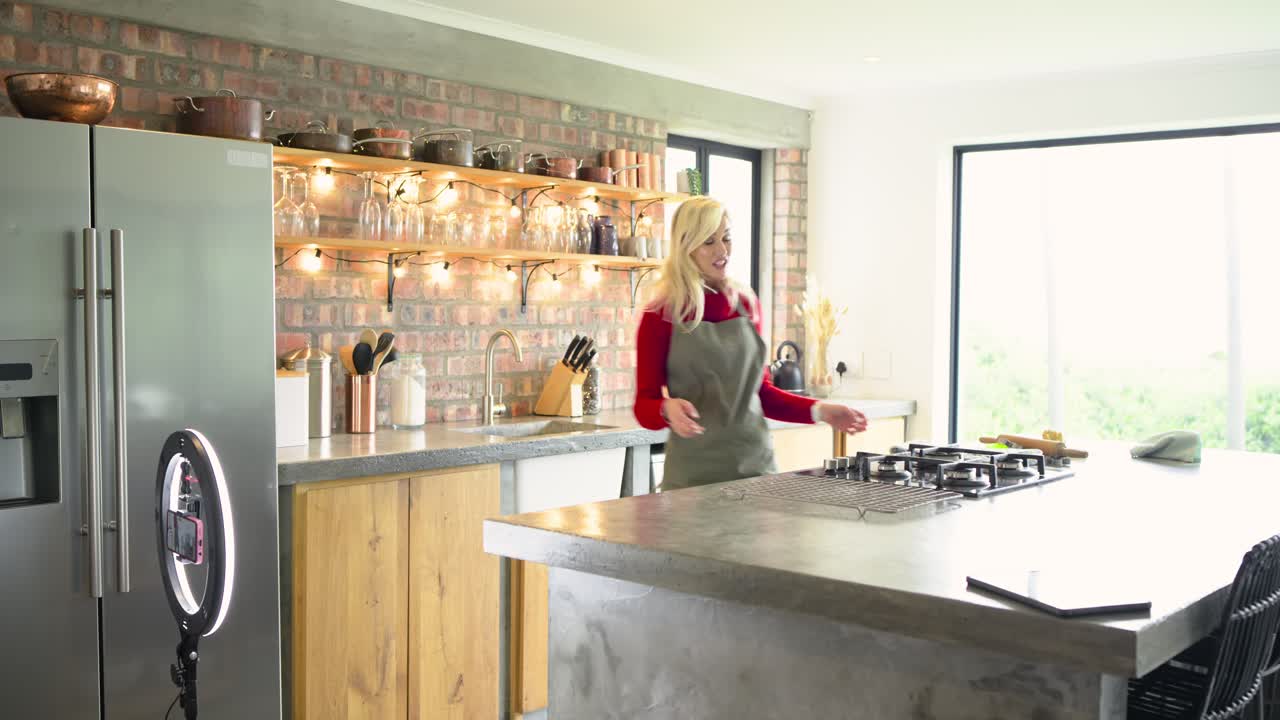 Woman entering kitchen, placing phone and adjusting ring light, showing grill rack and baking mat
