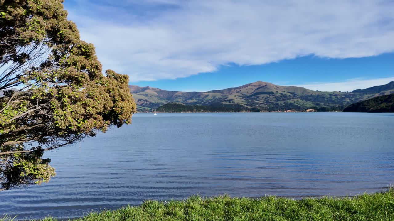 Aerial footage captures Akaroa's serene lake and surrounding mountains under clear skies, showcasing natural beauty and calmness