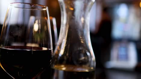 a focused view of a wine glass and carafe on a dimly lit table.