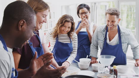Female-Teacher-Flipping-Flatbread-Pan-In-Cookery-Class-With-Adult-Students-Looking-On