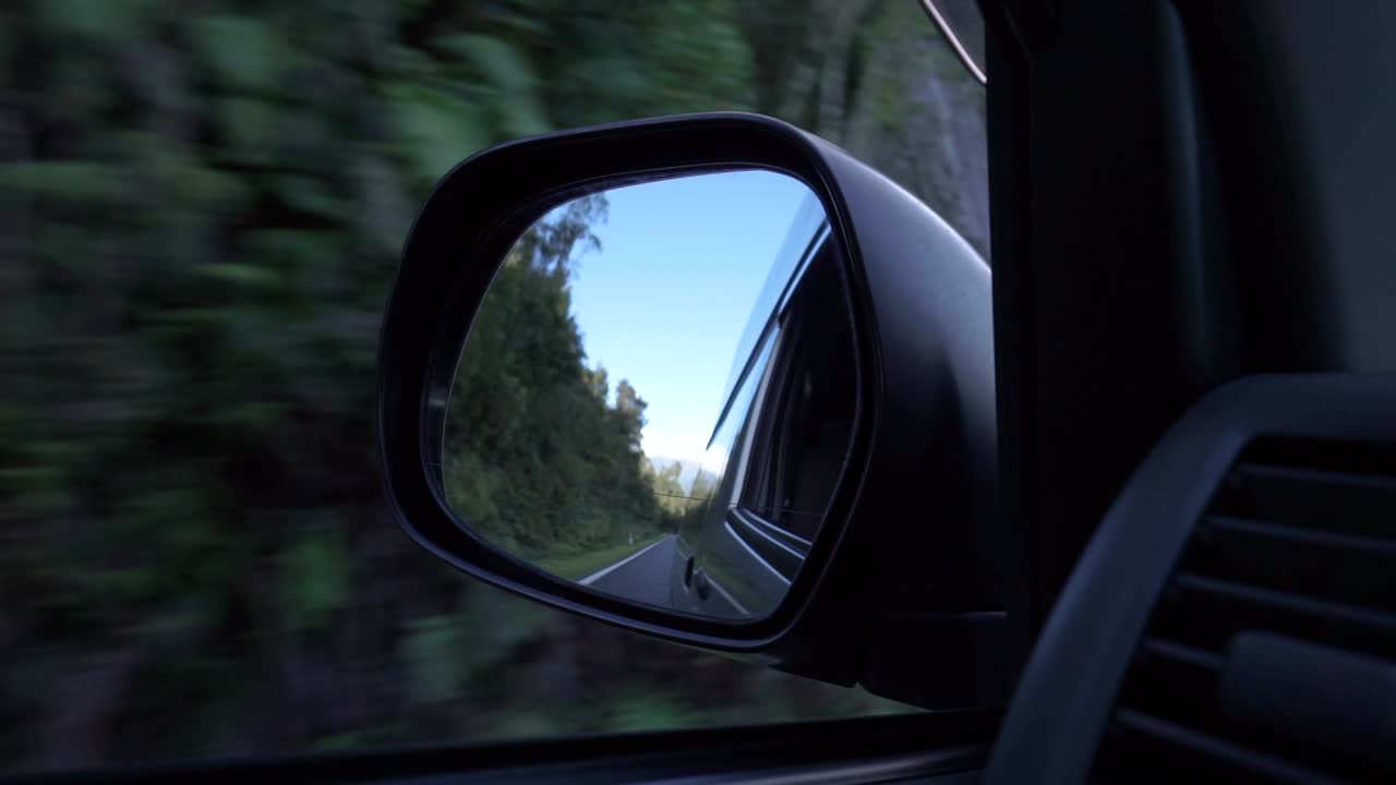 cámara lenta - automóvil conduciendo por la costa oeste, espejo retrovisor de nueva zelanda con montañas, árboles y cielo azul