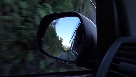 cámara lenta - automóvil conduciendo por la costa oeste, espejo retrovisor de nueva zelanda con montañas, árboles y cielo azul