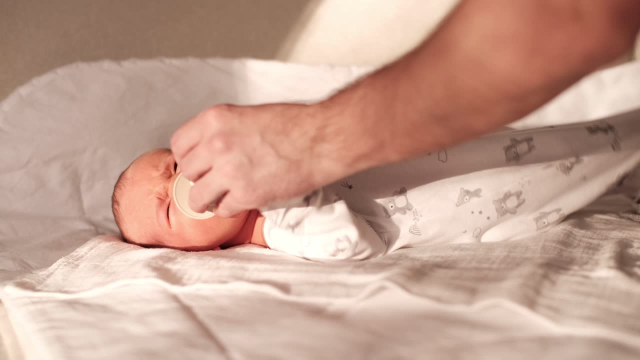 혼자 사는 아버지는 아기를 진정시켜 주머니를 입에 넣고, 회색 담요로 고, 손바닥으로 얼굴을 마사지합니다.