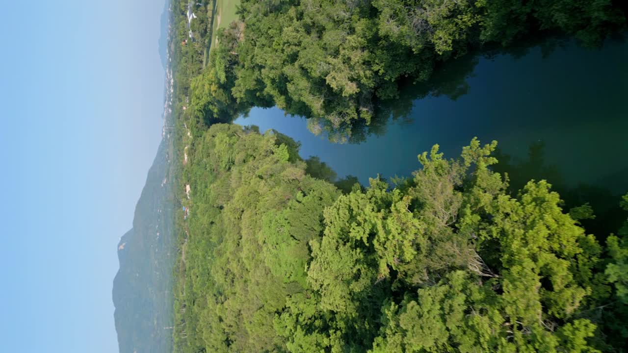 vuelo vertical aéreo sobre el pintoresco río muñoz durante el día soleado y el cielo azul rodeado de densos árboles forestales en la costa - paisaje montañoso en el fondo