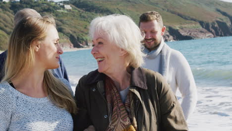 senior couple walking along shoreline with adult offspring on winter beach vacation