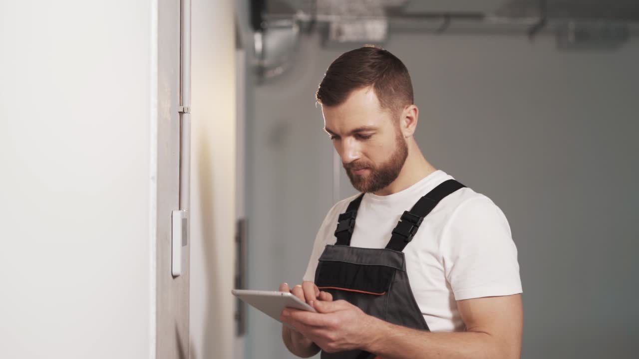 retrato de un hombre adulto con uniforme de trabajo con una tableta configurando el panel de control para seguridad, sistema de control de acceso, aire acondicionado e iluminación en una oficina moderna