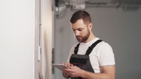 Portrait-of-an-adult-man-in-work-uniform-with-a-tablet-setting-up-the-control-panel-for-safety,-access-control-system,-air-conditioner,-and-lighting-in-a-modern-office