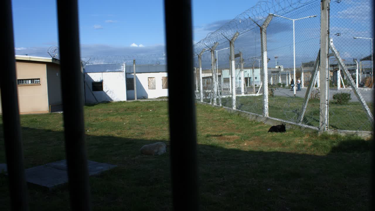 Veduta di un cortile carcerario attraverso sbarre di sicurezza e recinzioni.