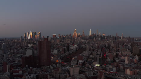 Fly-above-urban-neighbourhood-after-sunset.-Modern-downtown-skyscrapers-in-distance-reflecting-colourful-sunset.-Manhattan,-New-York-City,-USA