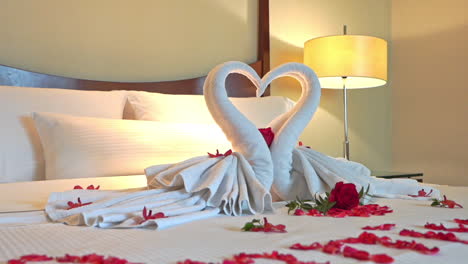 pan of linen sculpture of swans forming a heart on a bed covered with red roses and red rose petals