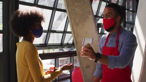 Trabajador-De-Café-De-Raza-Mixta-Con-Mascarilla-Tomando-La-Temperatura-De-Una-Compañera-De-Trabajo