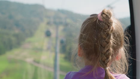 Cute-girl-with-ponytail-plait-turns-head-in-cabin-of-ropeway