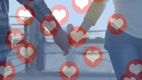 Multiple-red-heart-icons-floating-against-mid-section-of-couple-holding-hands-and-walking